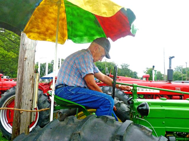 Driver seated under Beach Umbrella on vintage John Deere Tractor at Antique Tractor Exhibit